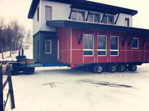 Blue and red housing modules in transit on McConnell Building Movers' high tech dolly pads.