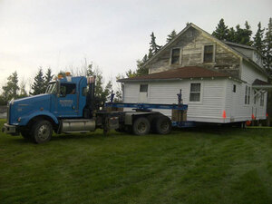 A muscular McConnell semi-tractor pulls a two-storey white house to it's new digs