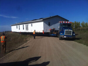 A dark blue McConnell truck moving a mobile home to it's final resting place.