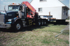 A large semi tractor with a cherry-picker on board towing a large house means McConnell Buuilding Movers of Central Alberta are on the job